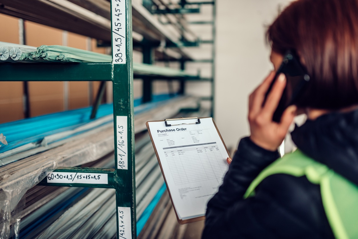 Female warehouse clerk using phone and looking at purchase order