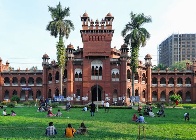 people sitting on a green grass field near a brown concrete building