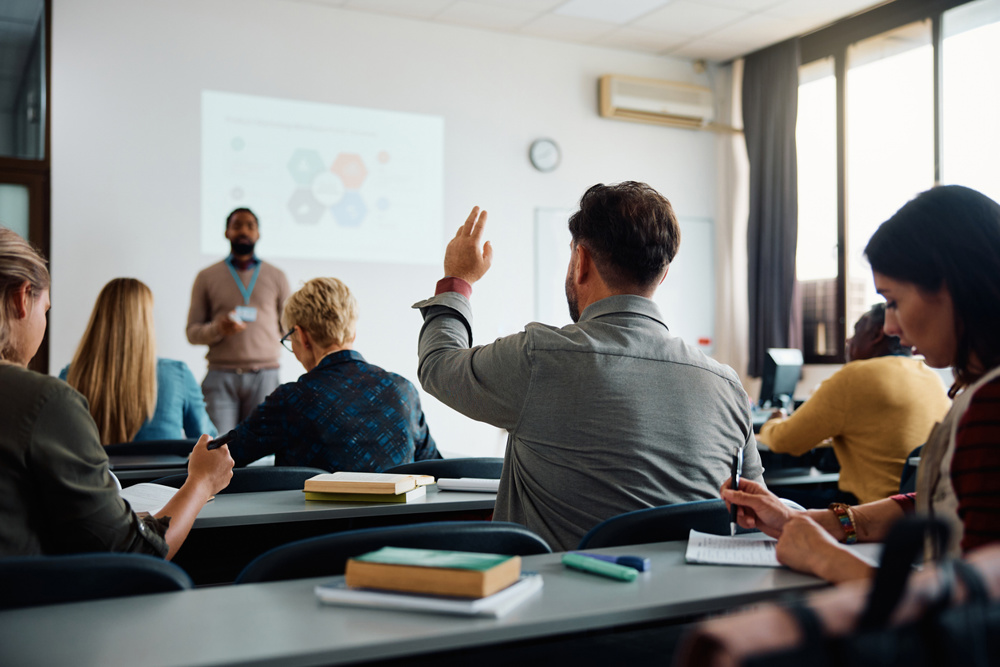 Rear view of man raising arm to ask a question during a presentation in lecture hall