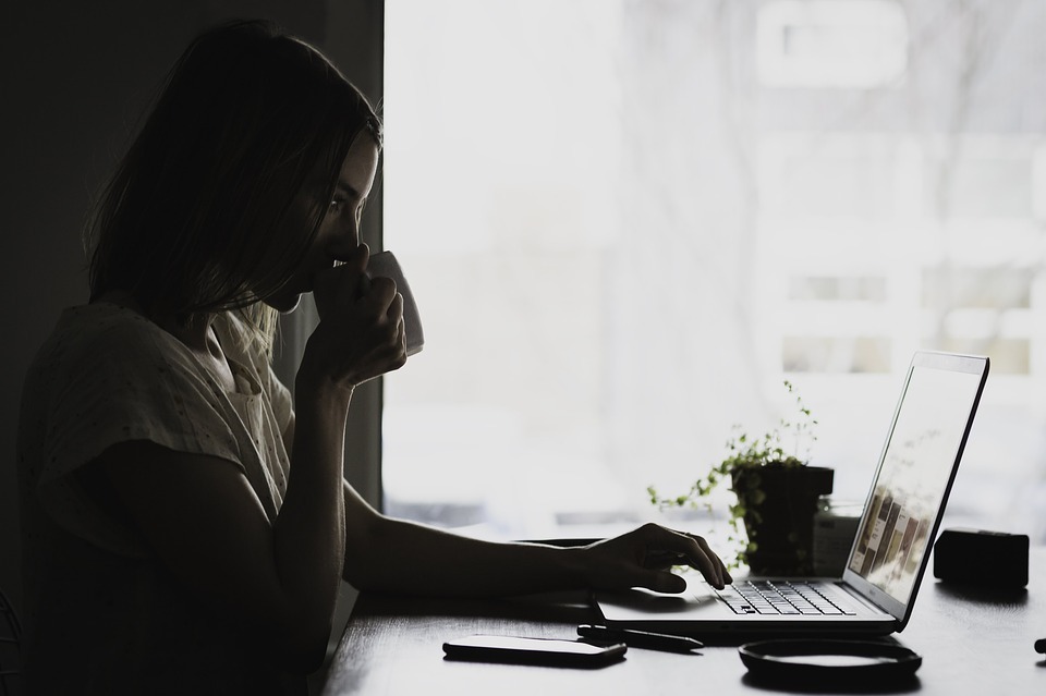 girl sipping in a cup, girl working in her laptop, plants, phone, pen sitting on the table