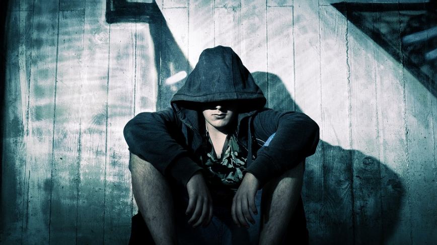 A man sitting with a hoodie covering his head with only his lips visible