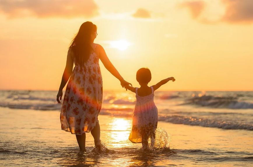 a mother and daughter walking at the beach, with the view of the sunset