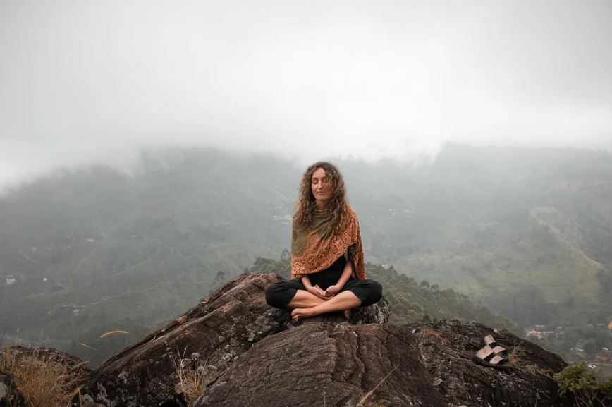 a woman cross-sitting at the top of a cliff, meditating