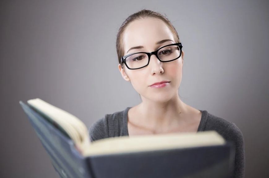 grey background, a woman reading a book, hardbound book, reading glasses