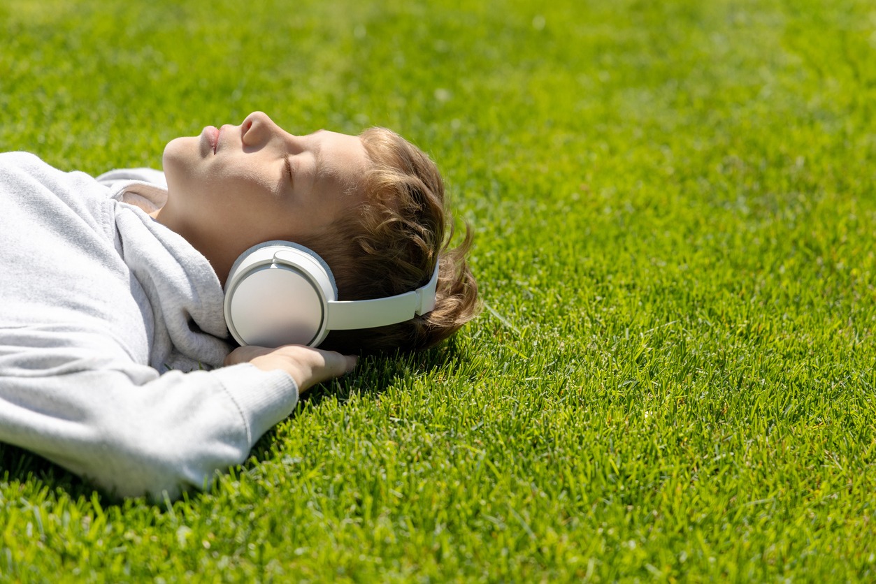 A boy relaxing on grass, listening to music with headphones