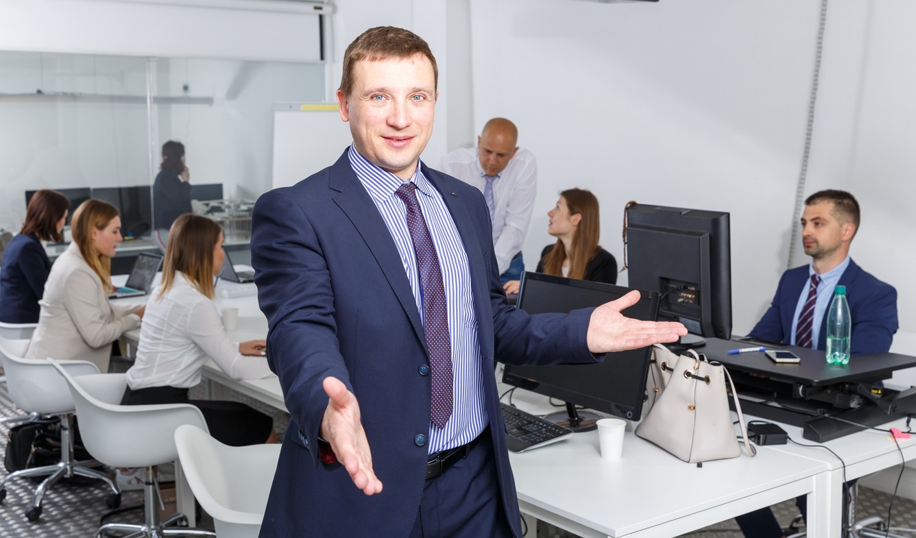 Successful businessman standing in office with open hand ready for handshake